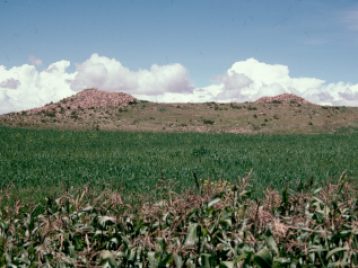 Large mound in the background with cloudy blue sky and grassland in the forefront.